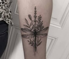 a black and white photo of a dragonfly tattoo on the right arm with flowers