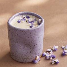 a cup filled with purple flowers sitting on top of a table next to some petals