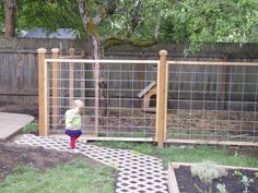 a small child standing in front of a fenced in area with grass and plants