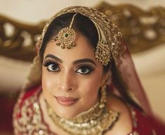 a woman in a red and gold bridal outfit with jewelry on her head, smiling at the camera