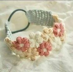 a crocheted headband with pink and white flowers sitting on top of a bed