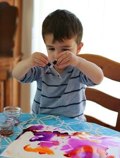 a young boy sitting at a table painting with watercolors on paper and glue