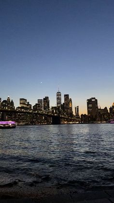 the city skyline is lit up at night with boats in the water and lights on