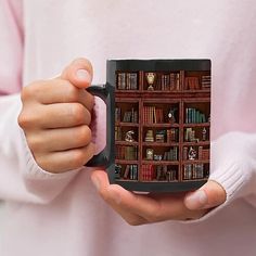 a person holding a coffee mug with bookshelves in the background on their hands