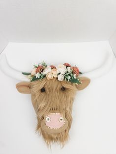 a cow with flowers on its head hanging from the ceiling in front of a white wall