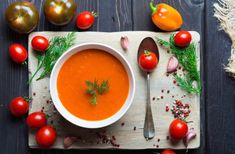 a bowl of tomato soup on a cutting board surrounded by tomatoes, garlic and herbs