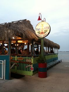 a tiki bar on the beach with people sitting in it