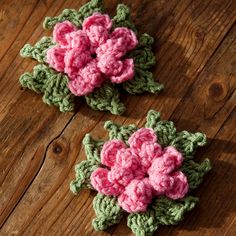 two crocheted pink flowers sitting on top of a wooden table next to each other