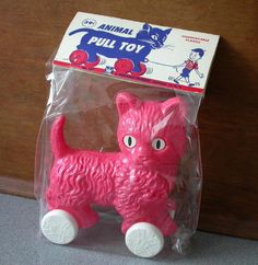 a pink plastic toy with wheels and a cat on it's back end, sitting in front of a wooden door