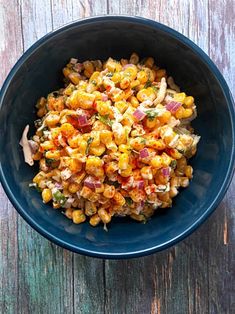 a blue bowl filled with corn salad on top of a wooden table