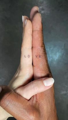 two hands holding each other with the word love tattooed on their thumbnails in front of them