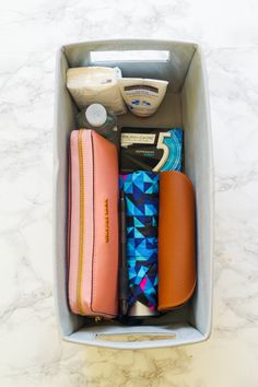 the contents of a travel bag are neatly organized in a gray container on a marble countertop