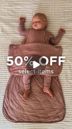 a baby laying on top of a bed with 50 % off select items