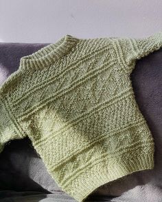 a green knitted sweater sitting on top of a couch