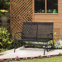 a black bench sitting in front of a wooden building with flowers around it and a green planter