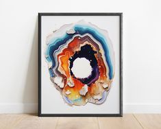 an abstract art piece in a frame on the floor next to a white wall and wooden floor