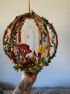 a hand holding up a wreath made out of branches and leaves with lights on it