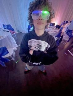 a young boy wearing sunglasses with green and blue light up glasses on his face, standing in a room full of chairs