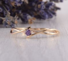 a gold ring with an amethorate stone in the center on a table next to purple flowers