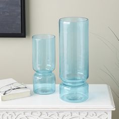 two blue glass vases sitting on top of a white table next to a book