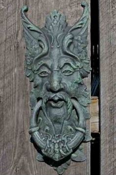 a metal door knockle with a face on it's side and a wooden fence in the background