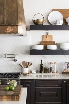 a kitchen with black cabinets and white marble counter tops, gold accents on the shelves