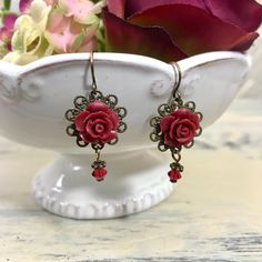 These dark red rose dangle earrings are so pretty and feminine. The resin roses are securely fastened onto antiqued brass filigree round discs with matching crystal drops. Earring wires are lead free hypoallergenic French wire hooks. Measures 1 1/2" long by 1/2" wide. Your beautiful earrings will come carefully packaged in a gift box and mailed with USPS Ground Advantage (formerly called First Class Mail) in a padded envelope with tracking. Jewelry Care: To keep your handmade earrings looking lo Dark Red Roses, Botanical Jewelry, Rose Jewelry, French Wire, Crystal Drop, Rose Earrings, Dark Red, Handmade Earrings, Jewelry Care