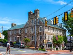 a man crossing the street in front of an old brick building with a green roof