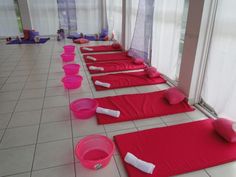 there are many red mats lined up on the floor with pink bowls and white towels