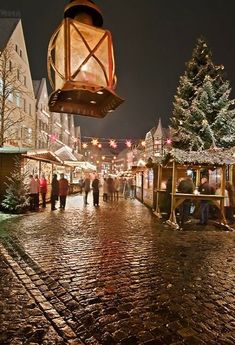 people are walking down the cobblestone street at christmas time with lights and decorations