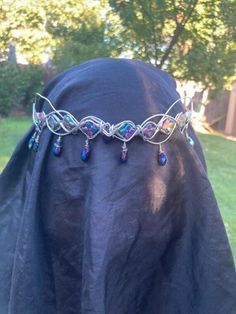 I made this crown with iridescent iris beads on the sides, with little iridescent blue/purple drop beads hanging from the sides, and an iridescent blue/purple bead in the center. The wire I used is high-quality silver anodized aluminum and won't rust or tarnish, but just to be safe, probably don't swim with this crown on. (: This crown, like all my others, fastens in the back with a brown suede leather cord, and is very flexible so you can shape it to your very unique head. The flexibility does mean that if you drop it, the crown will bend out of shape. Fortunately, the flexibility makes it easy to bend back into shape. This crown can be worn as shown in the picture, but I have seen many people who prefer to wear this kind upside down with the point of the stone facing up. This gives the c Elf Crown, Crown Silver, Iridescent Blue, Bleu Violet, Bridal Crown, Drop Beads, Costume Hats, Anodized Aluminum, The Wire