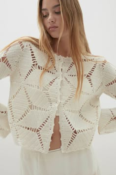 a woman wearing a white crochet sweater with openwork on the shoulders and back