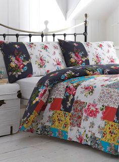 a bed with a floral quilt on it and a white trunk in the corner next to it