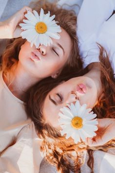 two young women laying on top of each other with white flowers in their hair and one has her eyes closed