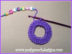 a crochet necklace with a purple circle hanging from it's end next to a knitting needle