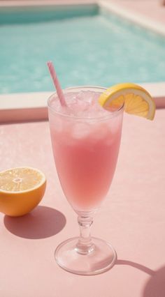 a pink drink sitting next to an orange near a swimming pool