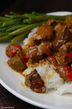 a white plate topped with meat and rice covered in sauce next to asparagus