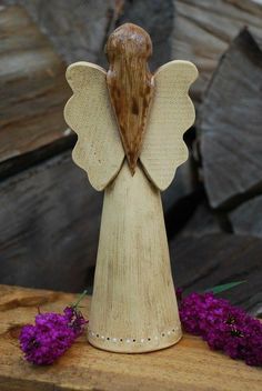 a wooden angel figurine sitting on top of a table next to purple flowers