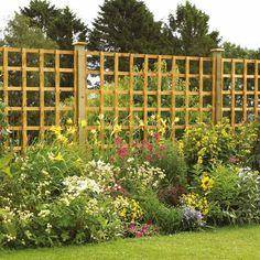 a garden filled with lots of flowers next to a tall wooden trellis on top of a lush green field