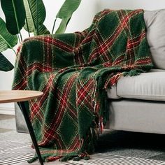 a green and red plaid blanket sitting on top of a couch next to a potted plant