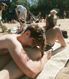 a man and woman laying on the beach with people in the background looking at their cell phones