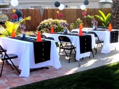 an outdoor party with white tablecloths and black tables topped with orange cone decorations