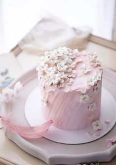 a pink frosted cake with white flowers on the top is sitting on a plate