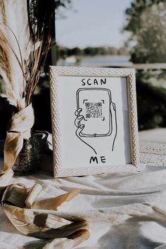 a white frame sitting on top of a table next to a vase and some dried plants