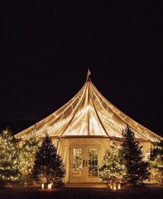 a large tent with christmas lights on it and trees in the foreground at night