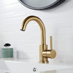 a gold faucet in a white bathroom with a round mirror above the sink