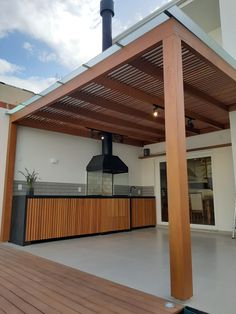 an outdoor kitchen with a wood stove and grill on the back deck, under a pergolated roof