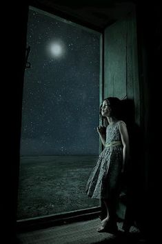 a woman standing in front of a window looking out at the night sky and stars