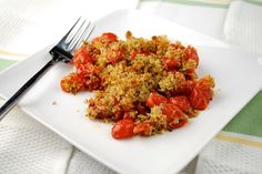 a white plate topped with crumbs and tomatoes next to a knife and fork