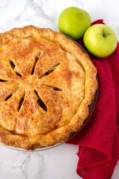 an apple pie sitting on top of a table next to two green apples